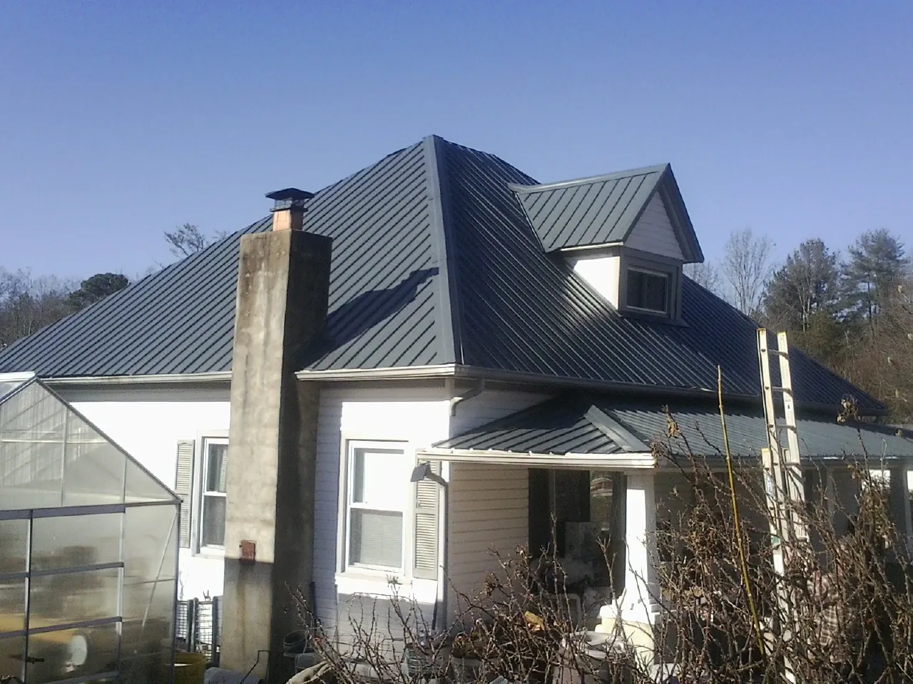 Dark blue standing seam metal roof on a white farmhouse with dormer — Slate & Tile Roof Repair by Roofing Brothers in South Vienna