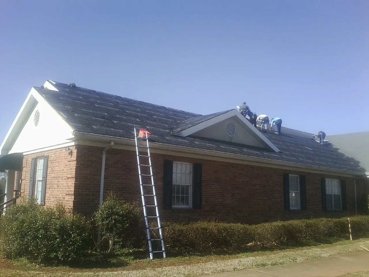 Crew tearing shingles off a brick ranch roof with a ladder set — Emergency Roof Repair work by our crew in South Vienna