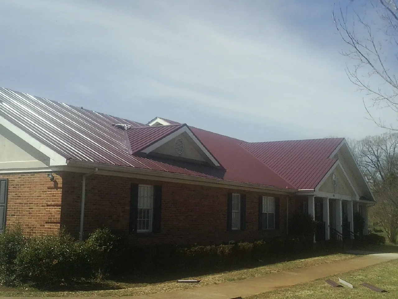 Red metal roof with gabled entries on a long brick building, from a Hail Damage Roof Repair job in South Vienna