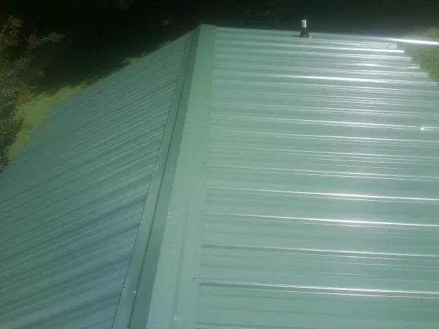 New green metal panels meeting at the ridge of a roof — Flat Roof Repair work by our crew in South Vienna