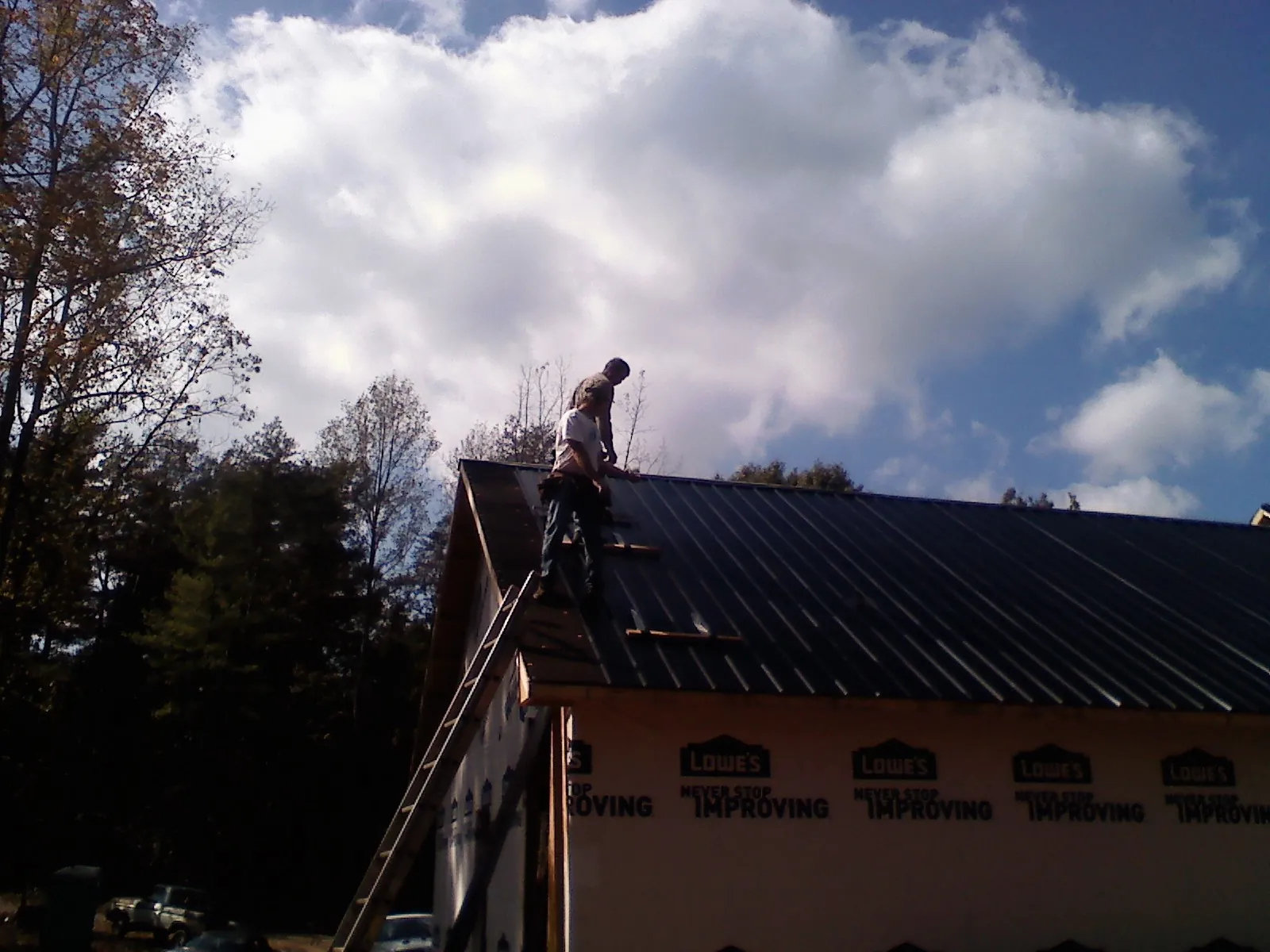 Roofer fastening dark metal panels high against a cloudy sky, from a Roof Inspection job in South Vienna