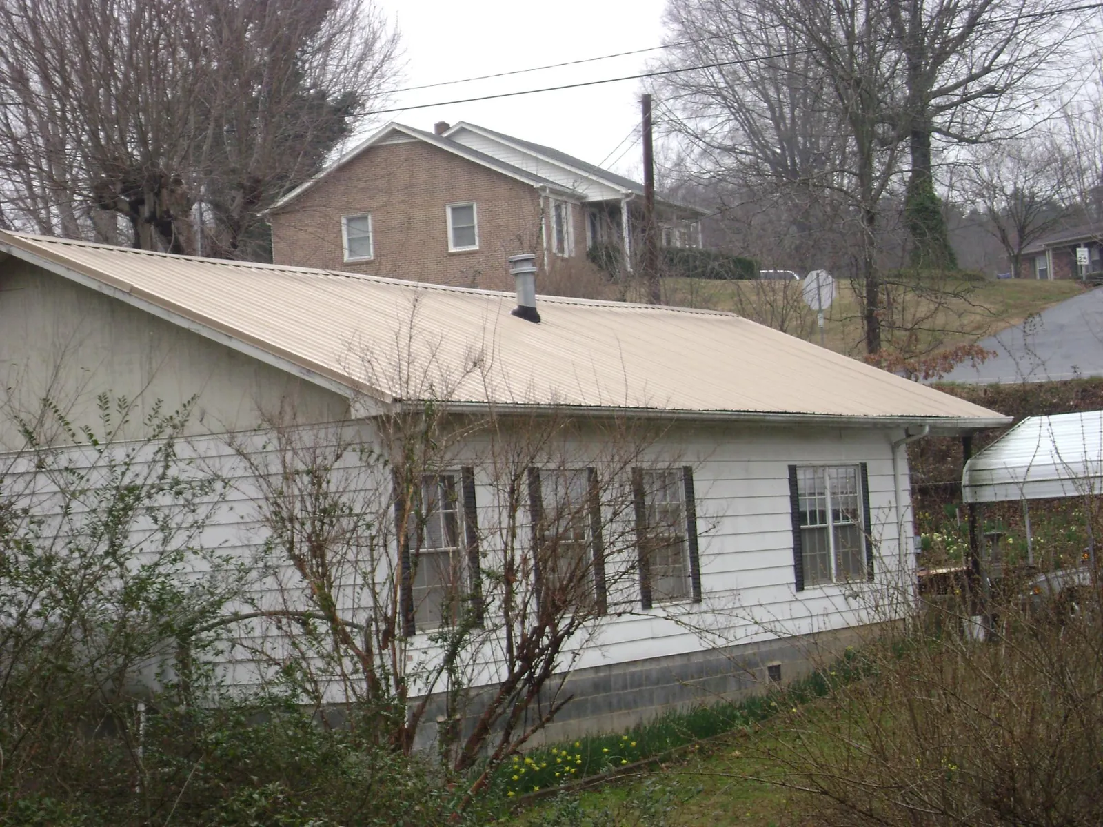 Tan metal roof on a white sided house set into a hillside — Commercial Roofing by Roofing Brothers in South Vienna